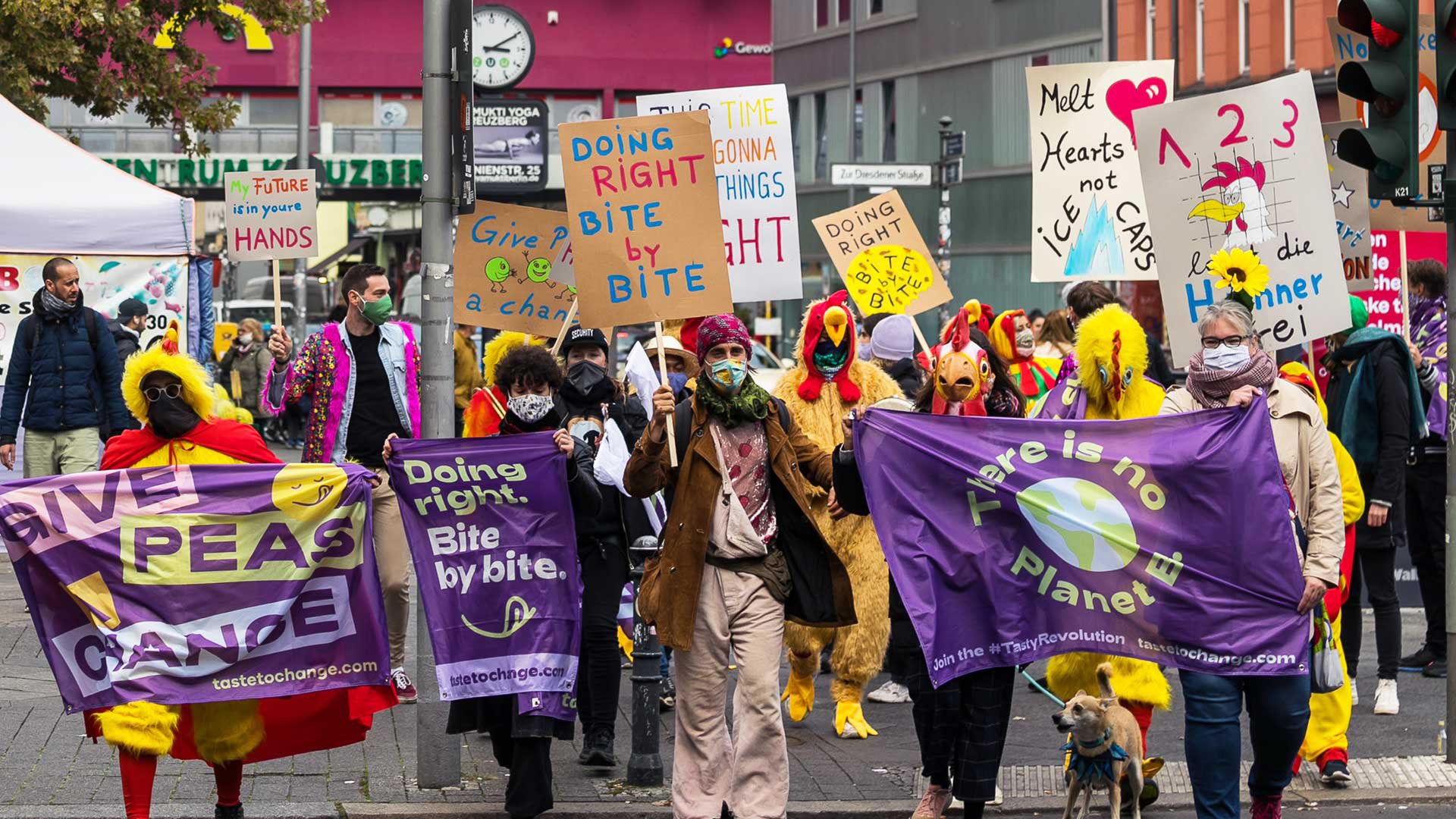 A crowd marching with purple 'There is no Planet B' and 'Doing right, bite by bite' flags